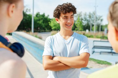 Gülümseyen ergenler el ele tutuşup kaykay parkında arkadaşlarıyla konuşuyorlar. Çocukların arkadaşlık konsepti
