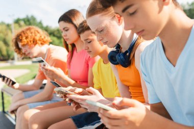 Şehirdeki sokakta oturan ve cep telefonuyla oynayan gençleri yakın çekim. Teknoloji bağımlılığı kavramı