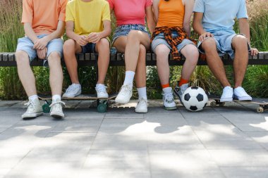 Bir grup gencin parkta elinde futbol topu ve kaykayla bankta oturması. Çocukların arkadaşlık konsepti