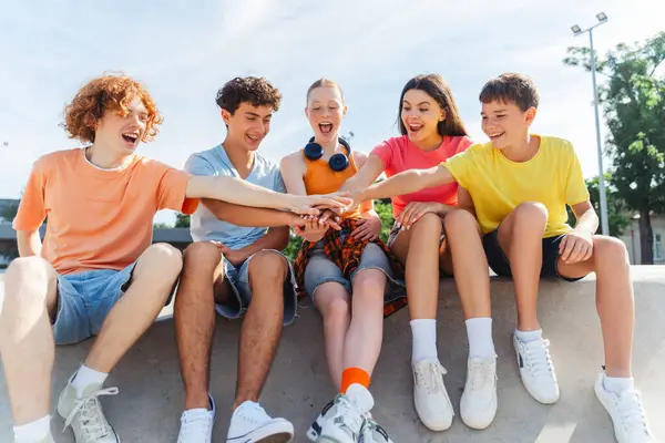 Stock image Excited friends, multiracial teenagers connecting hands, demonstrating spirit of friendship, sitting outdoors. Happy stylish boys and girls communication on the street. Friendship, positive lifestyle, summer