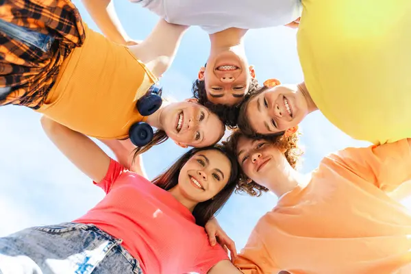 Mutlu gençler çember oluşturup gülüyorlar, sarılıyorlar ve kameraya bakıyorlar. Arkadaşlık kavramları, takım çalışması