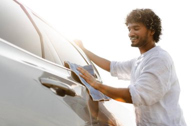 Genç adam güneşli bir günde arabasını mutlu bir şekilde yıkıyor. Sahiplik ve sorumluluk gururunu gösteriyor.