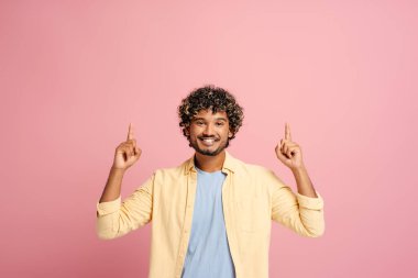 Genç yetişkin erkek model, pembe bir arka planda gülümserken işaret parmaklarıyla ekranın her iki tarafını işaret ediyor.