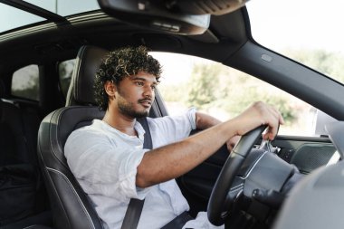 Kıvırcık saçlı genç adam güneşli bir günde modern arabasında özgürlüğün ve maceranın tadını çıkartıyor.