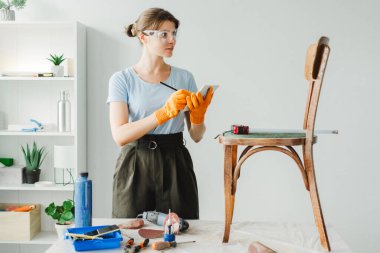 Güvenlik gözlüğü takan kadın marangoz atölyesinde klasik sandalye restorasyonunun yapılacaklar listesini yapıyor.