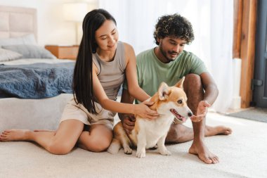 Çok ırklı bir çift, Corgi köpeklerini rahat bir yatak odasında severek evde rahat bir hafta sonu geçiriyorlar. Hayvan konseptine bayılırım.