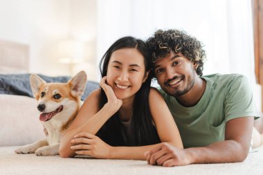 Genç, çok ırklı bir çift, Corgi köpekleri ile bir halıya uzanmış, rahat evlerinde rahatlatıcı bir anın tadını çıkarıyorlar. Aşk, hayvan, ilişki kavramı
