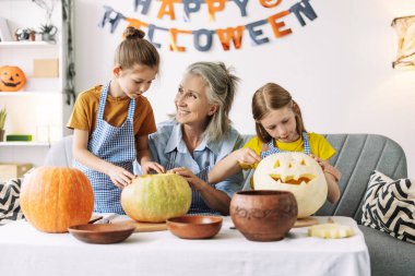 Grandmother and her granddaughters are carving pumpkins together for halloween, enjoying their time and creating spooky decorations clipart