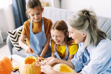 Büyükannen ve torunların gülümserken balkabağından tohum topluyorlar ve Cadılar Bayramı için balkabağı feneri oymaya hazırlanıyorlar. Kutlama konsepti
