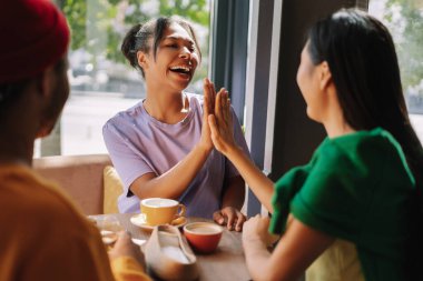 Üç genç kadın bir kafede kutlama yapıyor, beşlik çakıyor, iyi haberleri paylaşıyor, gülümsüyor, sohbet ediyor ve birlikte eğleniyorlar.