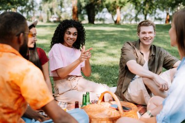 Parktaki yeşil çimlerin üzerinde dinlenen, gevşeyen, konuşan, toplanan, takım oluşturan, piknik yapan gülümseyen çok kültürlü arkadaşlar grubu. Çeşitlilik, arkadaşlık kavramı