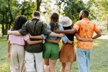 Beş genç yetişkinden oluşan bir grup bir parkta kollarını birbirlerinin omuzlarına dolayıp birlikte yürüyorlar. Hepsi gündelik kıyafetler giyiyor ve birbirlerine eşlik etmekten zevk alıyor gibi görünüyorlar.