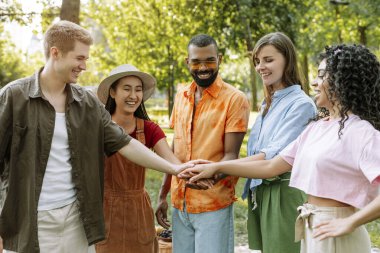Çeşitli genç yetişkinler parkta piknik yapıyor, güneşin altında kaynaşıyorlar. Gülümseyen, mutlu ve bağlı, takım çalışması ve birlik gösteriyorlar.