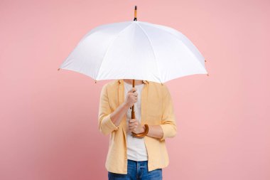 Genç adam yüzünü pembe bir arka planda beyaz bir şemsiyenin arkasına gizliyor, kopyalama alanı, maket. Reklam kavramı