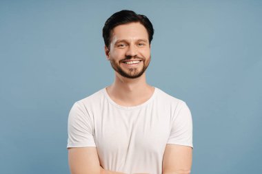 Sakallı, gülümseyen yakışıklı genç adam. Mavi arka planda izole edilmiş kameraya bakıyorum. Reklam kavramı