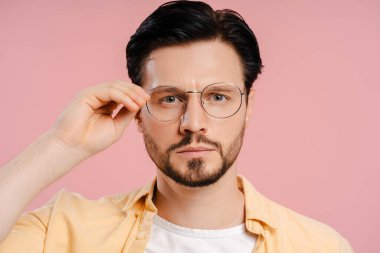 Ciddi bir adam pembe arka planda kameraya bakarak şık gözlükler takıyor. Görüş konsepti