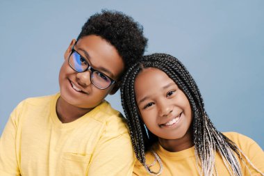 Gülümseyen Afrikalı Amerikalı çocuklar mavi arka planda izole edilmiş kameraya bakarak birbirlerine bağlanıyorlar. Çocukluk ve arkadaşlık kavramı