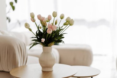 Taze kesilmiş laleli beyaz vazo, İskandinav iç dizaynı olan parlak bir oturma odasında bir sehpanın üzerinde duruyor.