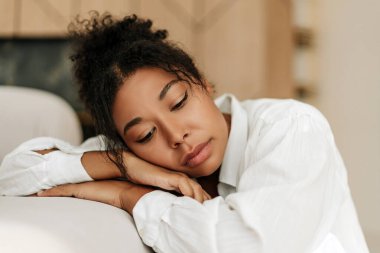 Üzgün bir ifadeyle genç siyahi kadın başını ellerinin üzerinde dinlendiriyor, yalnızlık ve tefekkür hissi taşıyor.