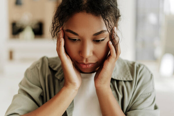 Молодая женщина держит голову руками, страдает головной болью, мигренью, стрессом или тревогой