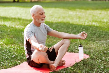 Son sınıf öğrencisi, güneşli yaz gününde parkta yoga antrenmanı yapıyor açık havada yoga minderinde oturuyor. Etkin yaşam tarzı kavramı