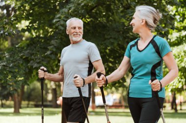 Mutlu, olgun bir çift, güneşli bir günün tadını çıkarır. Parkta yürüyen, gülümseyen ve çevresi yeşil ağaçlarla çevrili kuzeyliler. Etkin yaşam tarzı kavramı