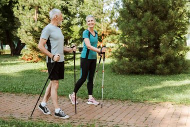 Yaşlı çift, parkta yürüyüş yaparak emekliliklerinin tadını çıkarıyor, gülümsüyor ve iyi vakit geçiriyorlar.