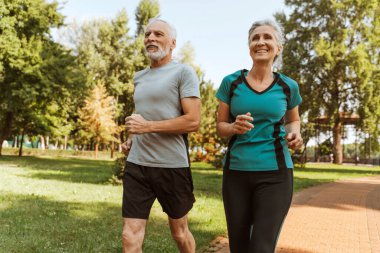 Çekici, gülümseyen son sınıf çifti spor giyerek parkta koşuyor ve sağlıklı bir hayat sürüyor. Spor konsepti