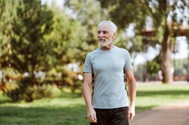 Çekici, gülümseyen, tişört giyen yaşlı bir adam parkta güneşli bir yürüyüşün tadını çıkarıyor, başka tarafa bakıyor. Başarılı konsept