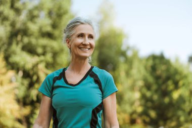 Kıdemli kadın parkta yaptığı egzersizden sonra rahatlıyor, doğada mutluluk ve memnuniyet yayıyor. Moda modeli dışarıda poz veriyor.