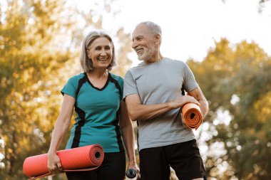 Erkek ve kadın birlikte spor yaparak aktif emekliliklerinin tadını çıkarıyorlar, yoga minderlerini tutuyor ve gülüyorlar. Sağlıklı yaşam tarzı kavramı