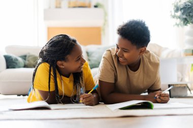 Mutlu erkek ve kız kardeş evde renkli kalemlerle resim çiziyor. Yerde birlikte yatan gülümseyen çocuklar. Hobi konsepti