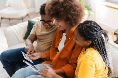 Mutlu Afrikalı Amerikalı kadın ve küçük çocuklar evde rahat bir koltukta oturup fotoğraf izlemenin keyfini çıkarıyorlar. Çocukluk, ebeveynlik kavramı