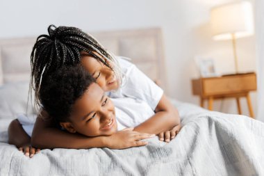 Karışık ırktan erkek ve kız kardeşler evdeki modern rahat odada yatakta sarılıyorlar. Çocukluk, akraba kavramı