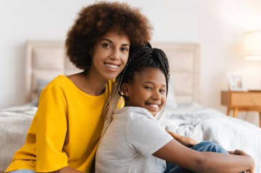 Afrika kökenli Amerikalı anne ve kızı yatak odasında kameraya poz veriyor. Çocukluk, annelik, aile kavramı.