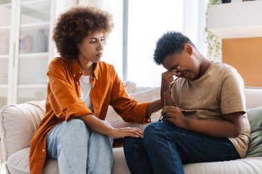 Ciddi bir anne, üzgün çocuğu oturma odasında kanepede otururken rahatlatıyor. Çatışan çocuklar ve ebeveynler. Kıvırcık anne konuşuyor. Genç bir çocuk yetiştirmede zorluklar.