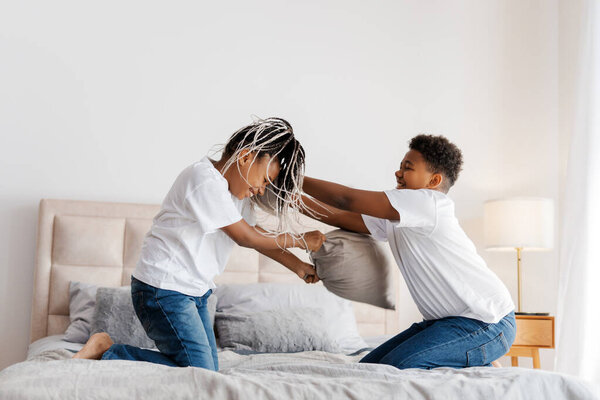 Portrait of smiling two siblings playing together with pillows, sitting on bed at home. Childhood, relatives concept