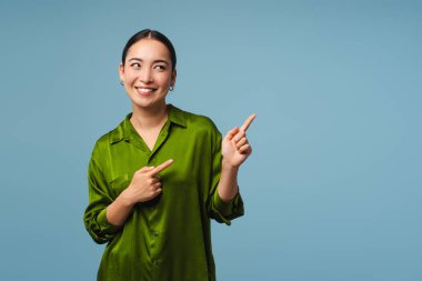 Güzel, gülümseyen Asyalı kadın mavi arka planda parmaklarını gösterip gülümsüyor. Alışveriş, reklam konsepti.