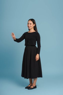 Gülümseyen, siyah elbise giyen, elleri mavi arka planda olan Asyalı bir kadın. Reklam kavramı