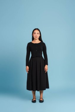 Güzel, çekici Asyalı kadın, kameraya bakıyor, mavi arka planda siyah elbise giyiyor. Reklam kavramı