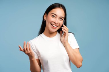 Gülümseyen, çekici Asyalı kadın konuşuyor, telefonlara cevap veriyor ve mavi arka planda el hareketleriyle işaret ediyor. İletişim konsepti