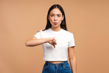 Çekici Asyalı kadın bej arka planda onaylanmamış baş parmak hareketi gösteriyor..