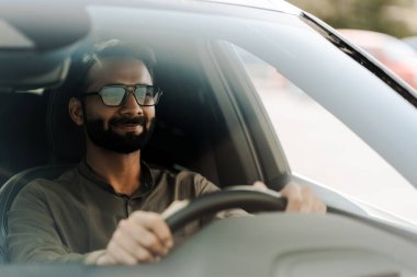 Güneş gözlüklü yakışıklı iş adamı güneşli bir günde arabasıyla gidip geliyor. Direksiyonu tutuyor ve kameradan uzağa bakıyor.