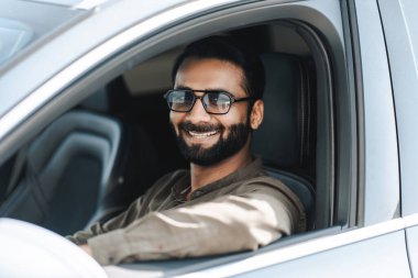 Hintli adam mutlu bir şekilde araba kullanıyor, şık güneş gözlüğü takıyor, güneşli bir günde neşe ve güven saçıyor. Özgür ve maceraperest hissetmek, kaygısız bir yaşam tarzını somutlaştırmak.