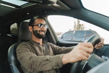 Güneşli bir günde arabasında gezen şık sakallı ve son moda güneş gözlüklü Hintli işadamı özgürlük ve neşe duygusuyla gülümsüyor ve yolculuğun tadını çıkarıyor.