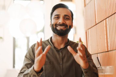 Pozitif Hintli adam video konferansı yapıyor, açıklama yapıyor, kameraya bakıyor. Çekici öğrenci çevrimiçi çalışıyor, video konferansı. Modern ofiste başarılı bir iş adamı çalışıyor.