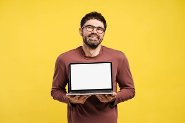 Gözlük takan mutlu bir Latin adam, elinde boş ekranlı dizüstü bilgisayar, maket, fotokopi odası, kameraya bakıyor, sarı arka planda tek başına duruyor. Reklam kavramı