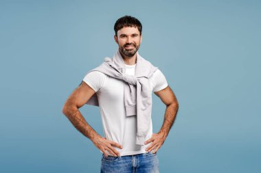 Gülümseyen, modern sakallı, sıradan kıyafetler giyen, mavi arka planda izole edilmiş kameraya bakan bir İspanyol. Moda modeli pozu. Reklam kavramı