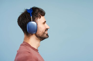 Yan görüş, gülümseyen sakallı adam, kulaklıkla müzik dinleyen, fotokopi alanına bakan, mavi arka planda tek başına duran. Reklam kavramı