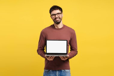 Gülümseyen, gözlüklü çekici Latin adam, elinde boş ekranlı dizüstü bilgisayar, fotokopi odası, kameraya bakan, sarı arka planda tek başına duran. Reklam kavramı